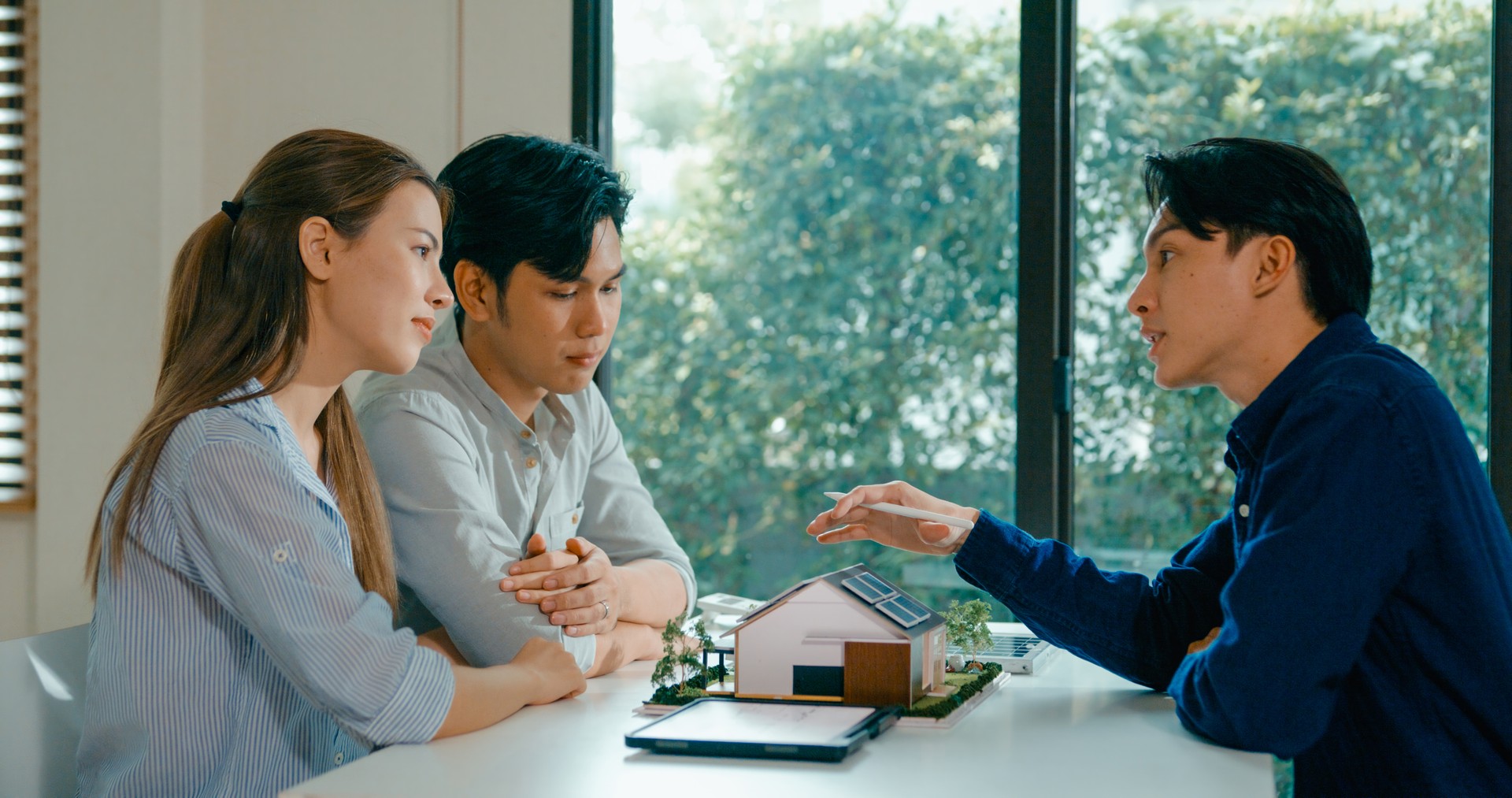 Young Asian couple in detailed consultation with real estate agent, who is highlighting advantages of home with solar panels. Consulting on Eco-Friendly Home Ownership with Real Estate Agent.